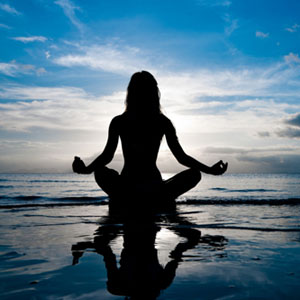 Woman meditating on the beach at sunrise